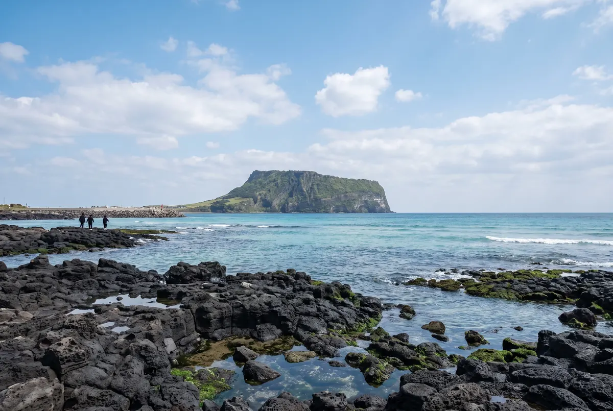 Black volcanic rocks on the Jeju coast with Seongsan Ilchulbong in the distance